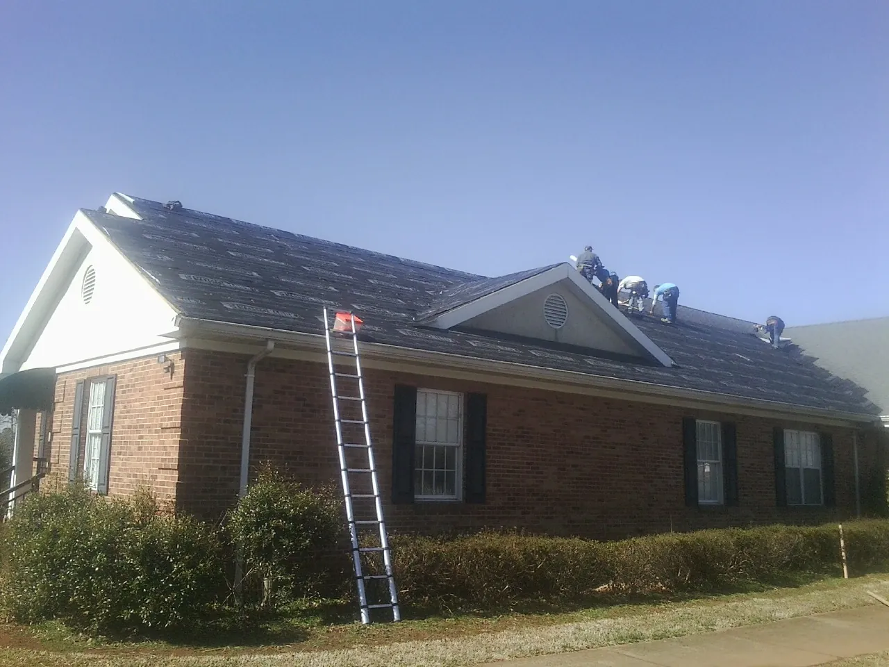 Crew tearing shingles off a brick ranch roof with a ladder set — Emergency Roof Repair work by our crew in New Middletown