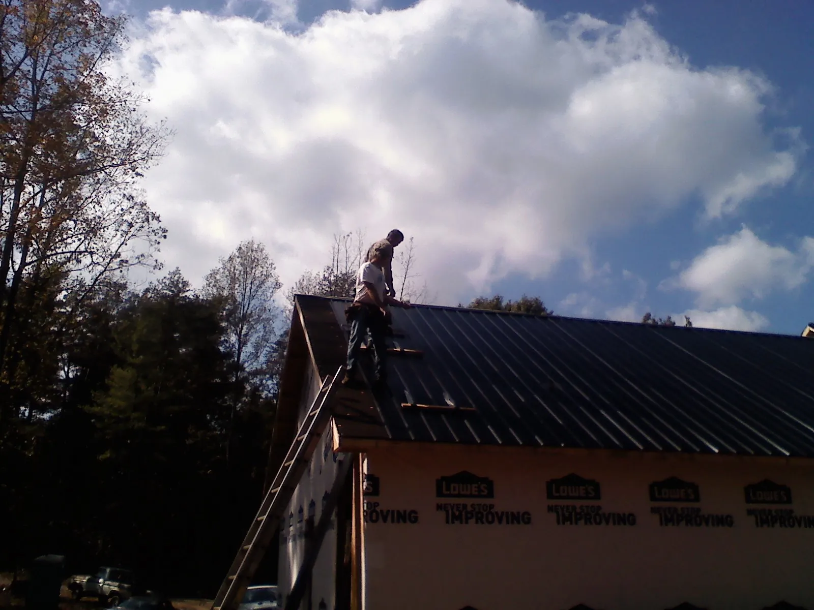 Roofer fastening dark metal panels high against a cloudy sky, from a Roof Inspection job in New Middletown