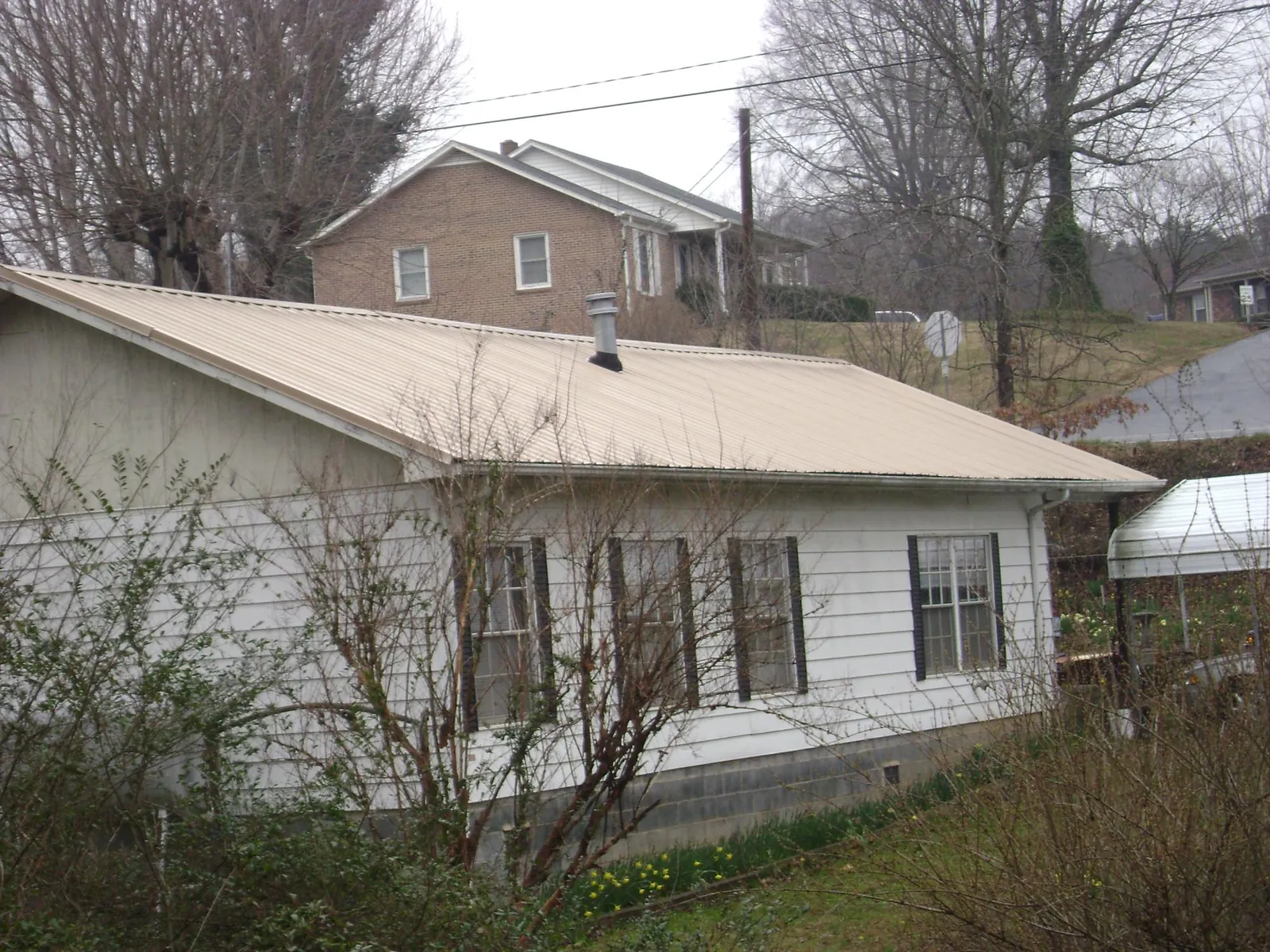 Tan metal roof on a white sided house set into a hillside — Commercial Roofing by Roofing Brothers in New Middletown